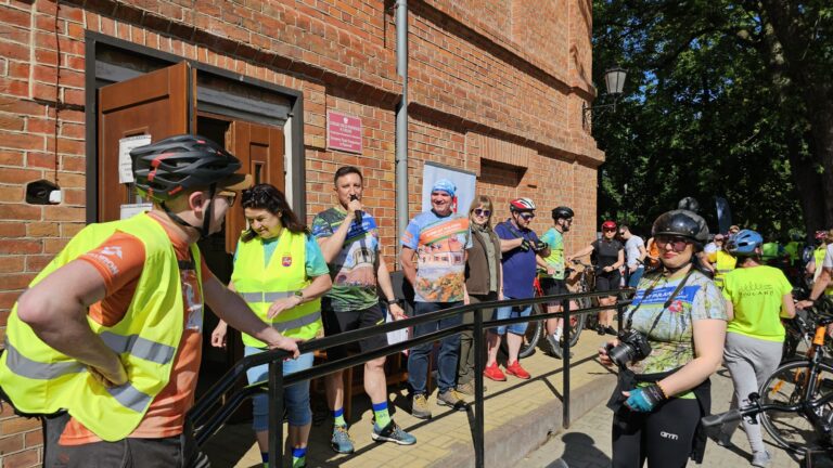 Osoby w kamizelkach odblaskowych i rowerzyści przed startem rajdu rowerowego